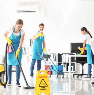 Three cleaning professionals in blue aprons using cleaning equipment in an office environment with a caution sign for wet floor.