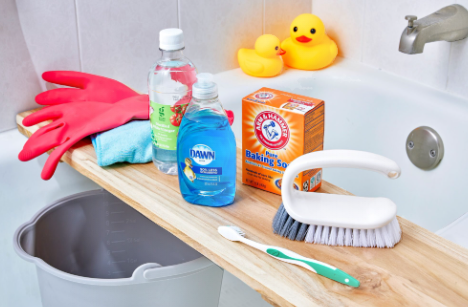 Bathroom Cleaning in Pittsburgh. Cleaning supplies including Dawn dish soap, baking soda, a scrub brush, and rubber gloves on a bathtub ledge.
