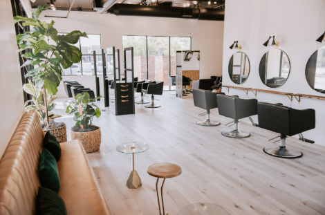 Interior of a modern hair salon featuring black styling chairs, mirrors, and a plant.
