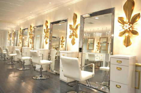 Interior of a modern salon featuring multiple mirrors and white styling chairs with gold accents.