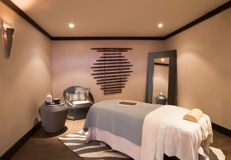 Spa treatment room with a massage table, decorative wall art, and a mirror reflecting the space.