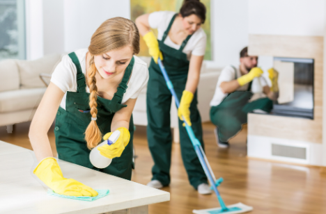 Three cleaning professionals in green uniforms using cleaning supplies in a modern indoor setting.