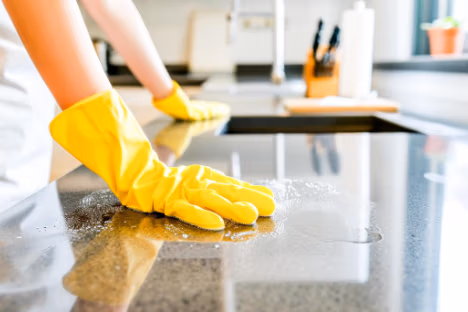 Kitchen cleaning services. Person wearing yellow rubber gloves cleaning a kitchen countertop with a cloth.