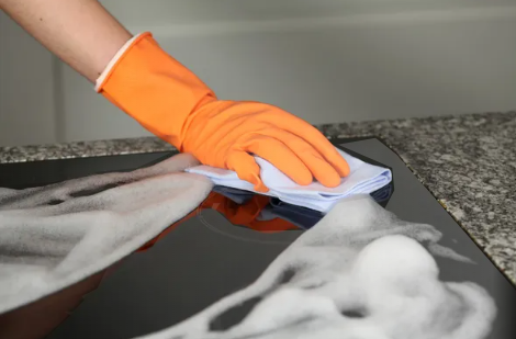 Kitchen Cleaning Services. Person wearing orange rubber gloves cleaning a surface with a cloth and foam.
